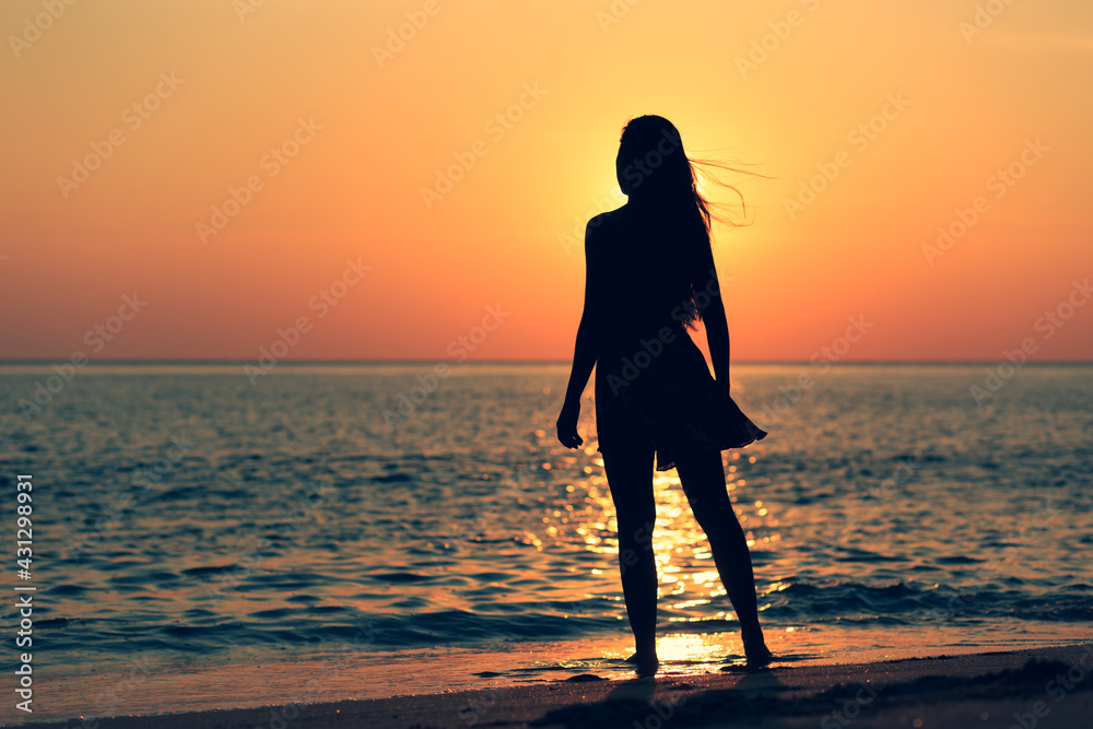 Silhouette woman dancing at sea, ocean during summer sunset on blurred background.