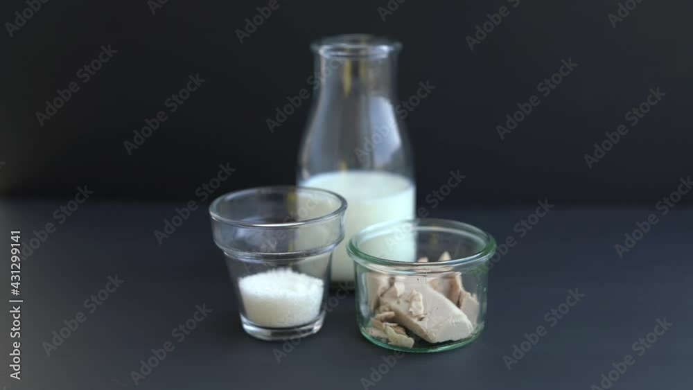 Hand of chef putting glass of milk on black table. Yeast dough starter ingredients concept: milk, sugar and fresh wild yeast in transparent glasses on black background. High quality 4k video footage Hand of chef putting glass of milk on black table. Yeast dough starter ingredients concept: milk, sugar and fresh wild yeast in transparent glasses on black background. High quality 4k video footage