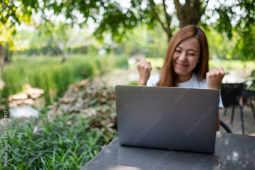 A young asian woman celebrating success while working on laptop computer in the outdoors