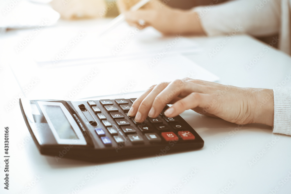 Accountant checking financial statement or counting by calculator income for tax form, hands closeup. Business woman sitting and working with colleague at the desk in office. Tax and Audit concept Accountant checking financial statement or counting by calculator income for tax form, hands closeup. Business woman sitting and working with colleague at the desk in office. Tax and Audit concept