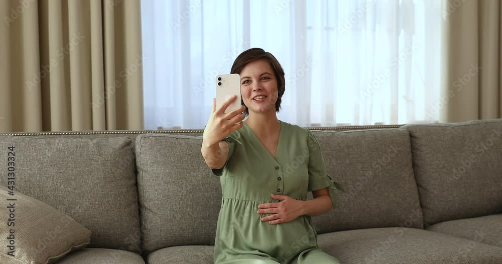 Happy pregnant woman talk via video conference app on smartphone, sit on sofa hold device having pleasant conversation use video call event, Virtual meeting with family, share news remotely concept Happy pregnant woman talk via video conference app on smartphone, sit on sofa hold device having pleasant conversation use video call event, Virtual meeting with family, share news remotely concept