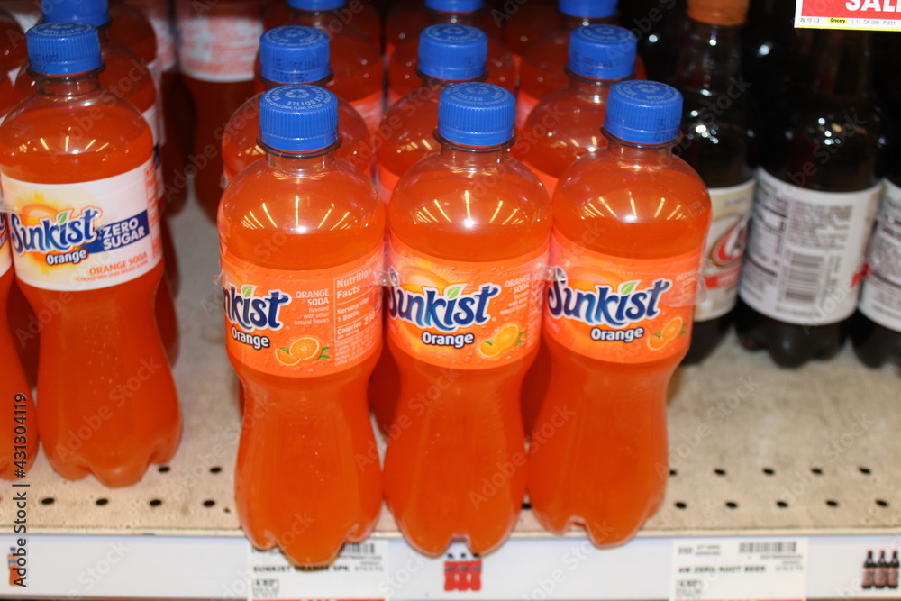 Orange Sunkist soda pop shot closeup on a metal shelf that's bright and