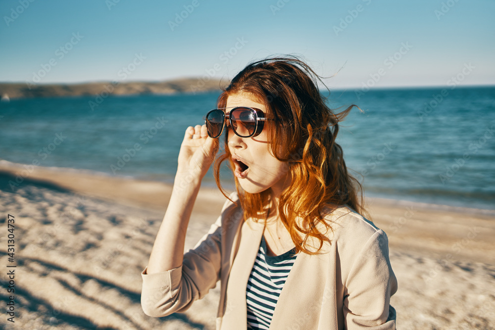 happy red-haired woman in beige jacket and t-shirt on the sand near the sea in the mountains happy red-haired woman in beige jacket and t-shirt on the sand near the sea in the mountains
