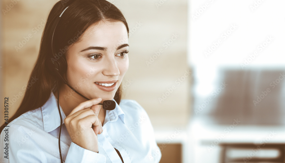 Brunette female customer service representative in a headset is consulting clients online. Call center and business people concept Brunette female customer service representative in a headset is consulting clients online. Call center and business people concept