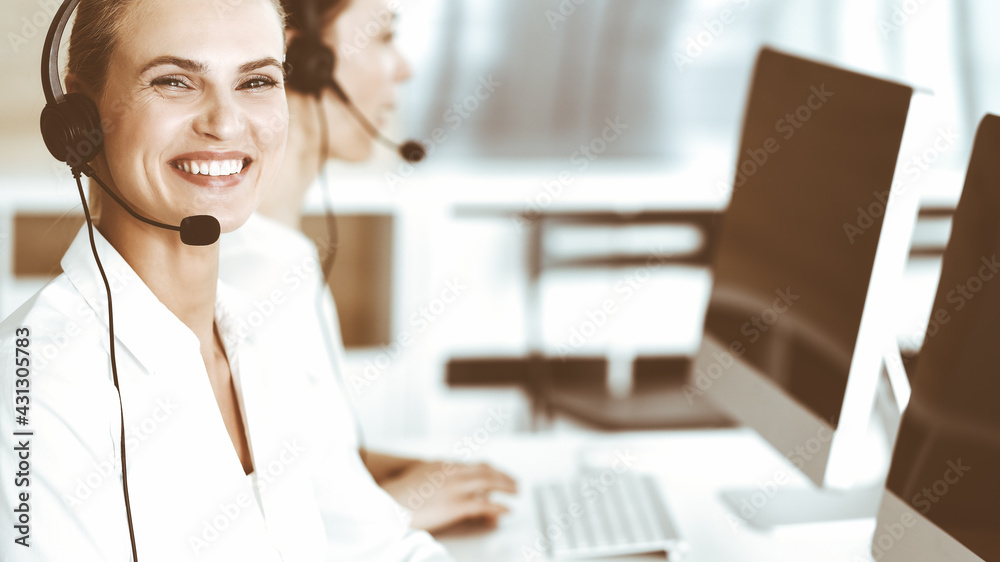 Blond female customer service representative and her colleague are consulting clients online using headset. Call center and business people concept Blond female customer service representative and her colleague are consulting clients online using headset. Call center and business people concept