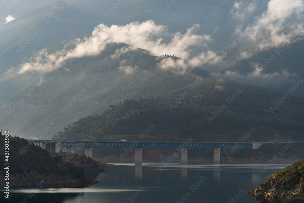 Truck driving over a bridge over a swamp surrounded by mountains and forests with low clouds.