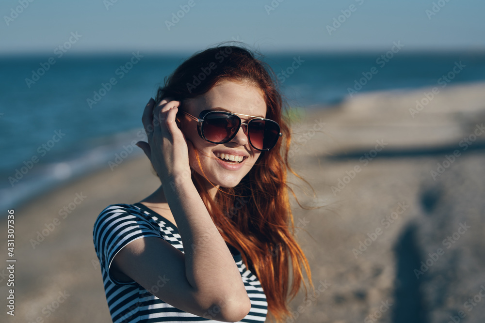 red-haired woman in the mountains in nature in glasses gestures with her hands on the beach near the sea red-haired woman in the mountains in nature in glasses gestures with her hands on the beach near the sea
