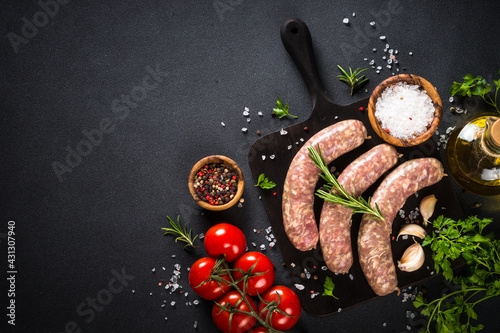 Bratwurst or sausages on cutting board with spices at black table.