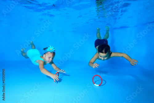 A little boy and girl swim and dive, and collect toys underwater from the bottom of the pool. Children's sports swimming. Portrait. Horizontal view.