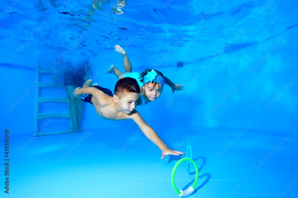 The children, a happy girl and boy, dive together to the bottom of the pool and collect toys underwater from the bottom. Portrait. Horizontal view.