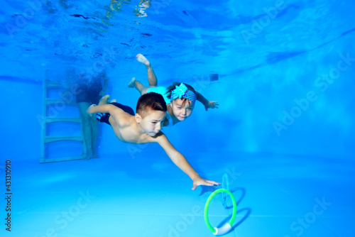 The children  a happy girl and boy  dive together to the bottom of the pool and collect toys underwater from the bottom. Portrait. Horizontal view.