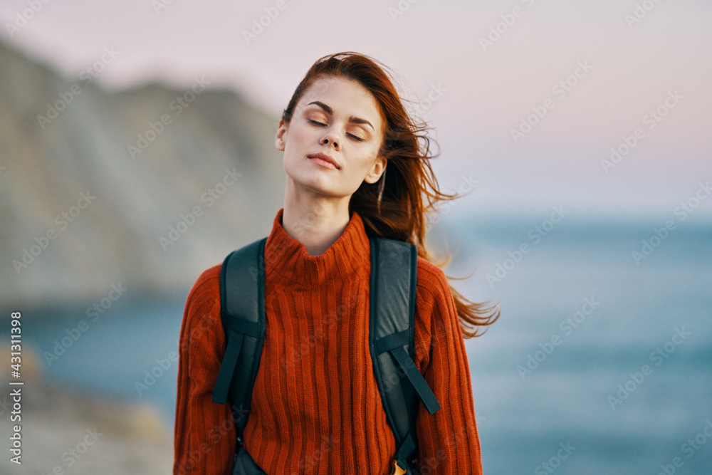 woman in a red sweater with a backpack on her back resting in the mountains outdoors near the ocean 