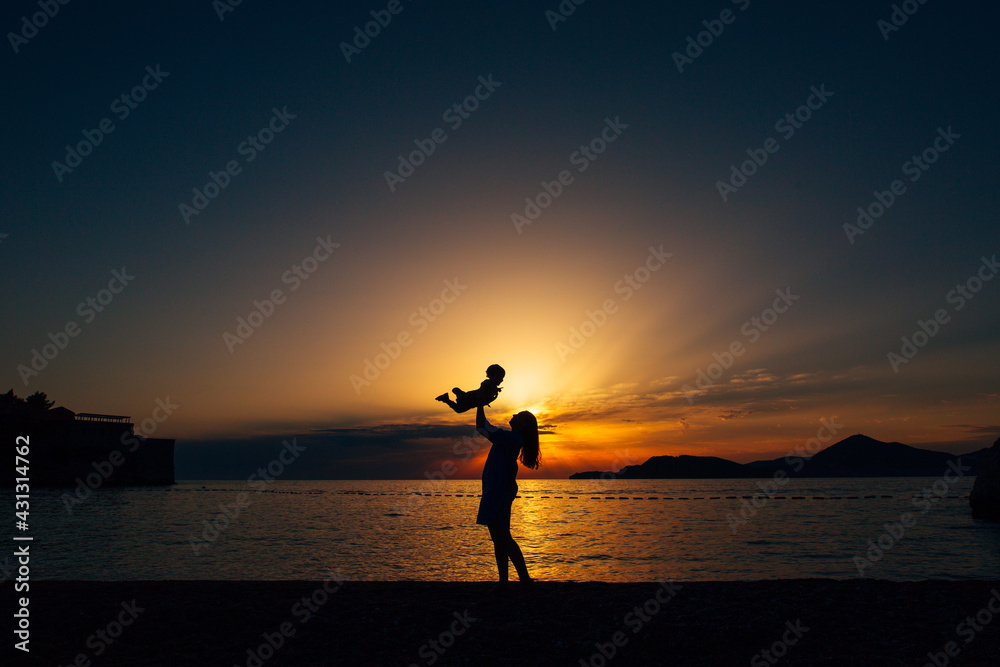 Mom throws up her little son and plays with him on the beach at sunset 