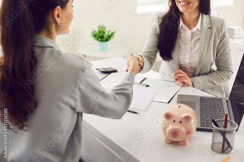 Cropped image of the handshake of two women of a bank agent and a client over a table with signed documents in the bank office. Concept of financing, lending, agreement and business ethics.