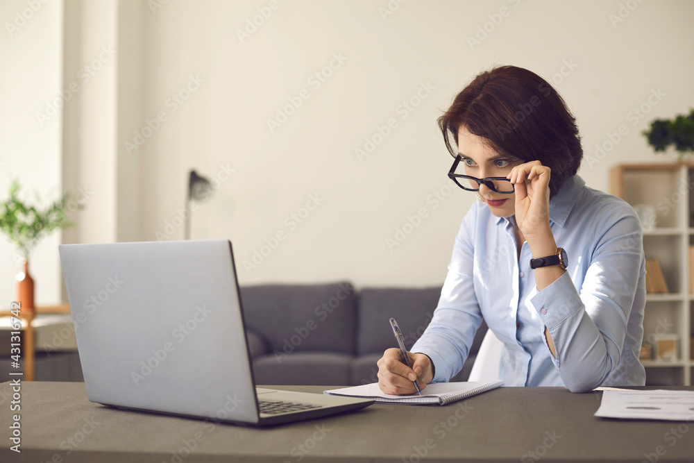 Distance learning at home. Woman looking at laptop computer screen takes off glasses in surprise. Adult student with attention to detail studying new information in online continuing education webinar Distance learning at home. Woman looking at laptop computer screen takes off glasses in surprise. Adult student with attention to detail studying new information in online continuing education webinar