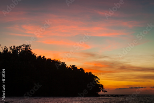 Vivid sunset sky waterscape and silhouette forest island