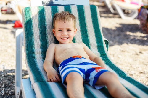 a boy of 4 years old in striped shorts lies on a sunbed on the beach, contented and happy. Summer, seashore