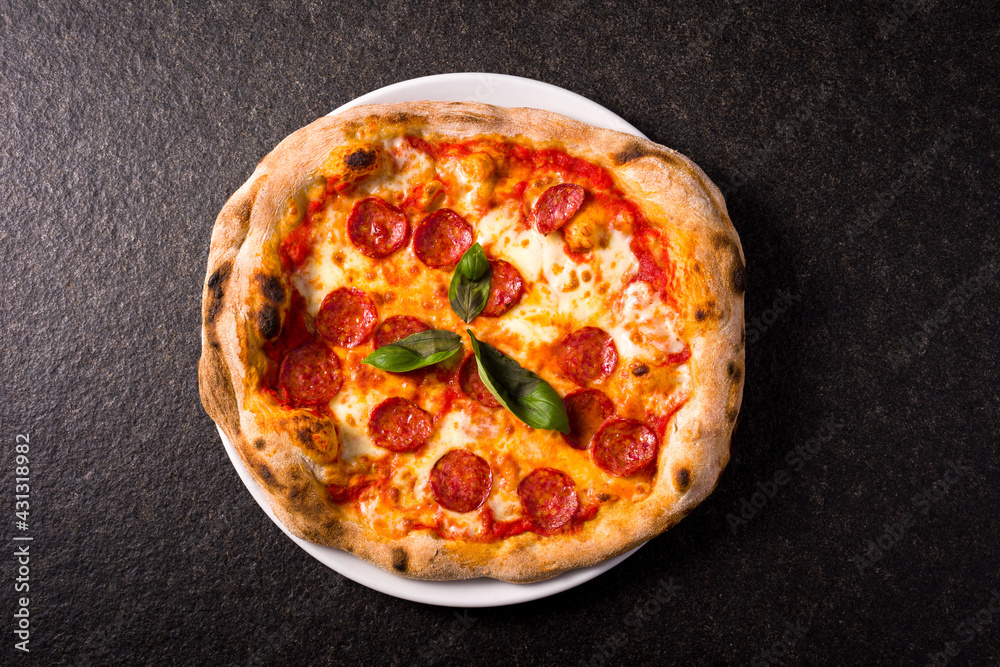 pizza alla diavola with spicy salami, mozzarella, tomato and basil. view from top. black stone background
