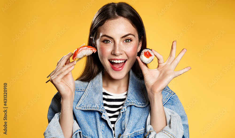 Happy woman shows sashimi and makizushi. Girl eating sushi rolls with chopsticks and smiling from amazing discounts for takeaway in japenese restaurant. Female student order lunch in delivery app Happy woman shows sashimi and makizushi. Girl eating sushi rolls with chopsticks and smiling from amazing discounts for takeaway in japenese restaurant. Female student order lunch in delivery app