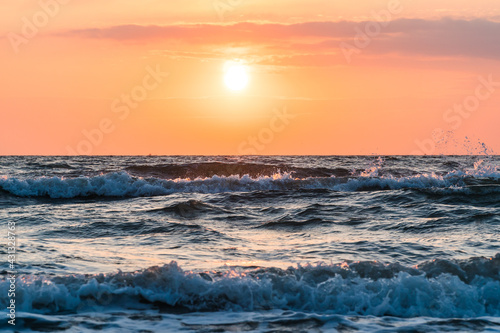 Close up of orange sunrise over the ocean with waves in the forground