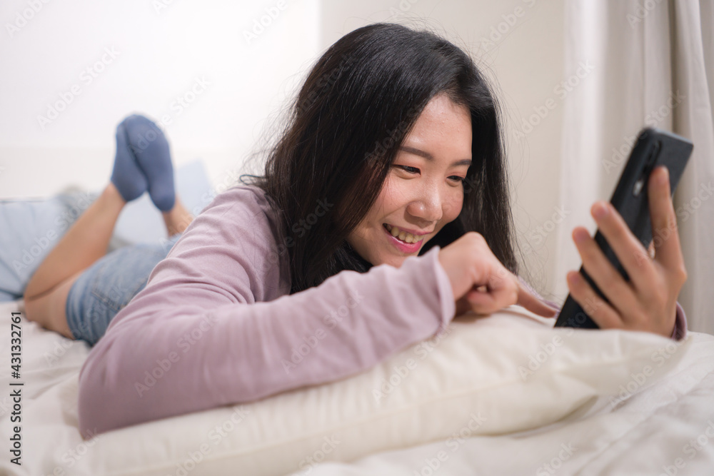 Asian girl with hand phone - home lifestyle portrait of young happy and attractive Chinese woman on bed using internet mobile internet app smiling cheerful in bedroom Asian girl with hand phone - home lifestyle portrait of young happy and attractive Chinese woman on bed using internet mobile internet app smiling cheerful in bedroom