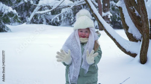 Little happy girl smiles and rejoices in winter. A child in the snow and drifts. A warm kerchief and a hat with a bumbon on a child in a winter park and forest. We meet winter. High quality 4k footage photo