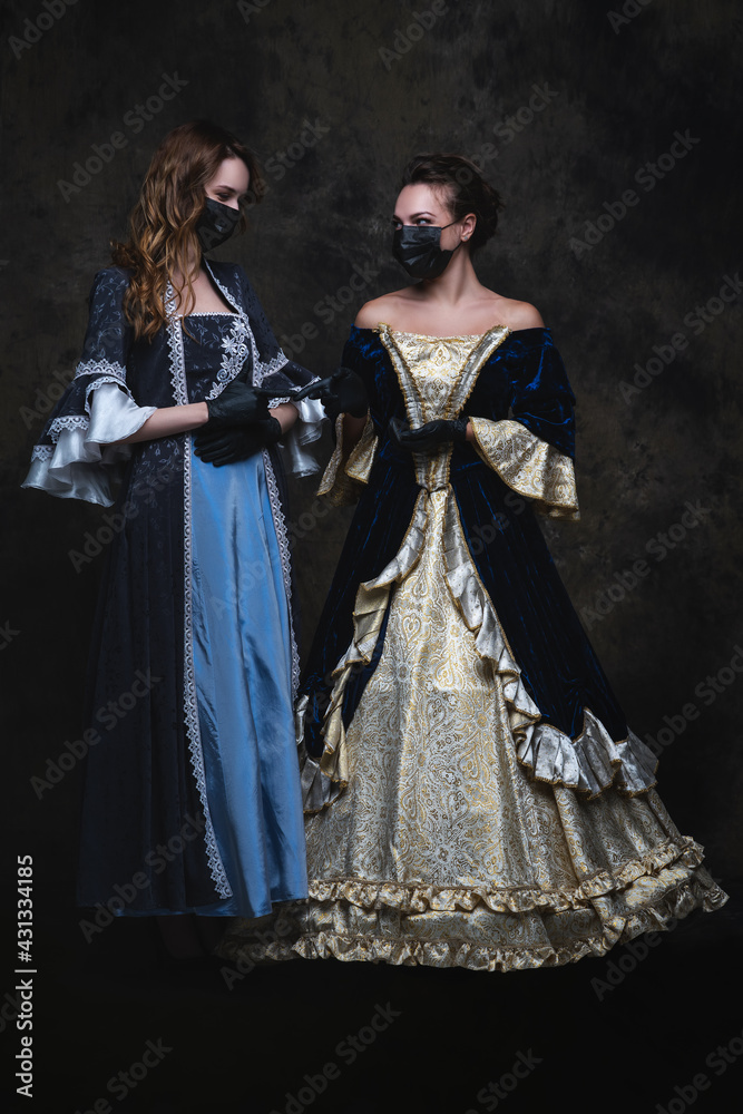 Two women in renaissance dress, face mask and gloves on abstract dark background, coronavirus, covid-19 protection concept