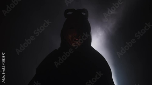 Creepy, masked cultist standing in a dark room. Scary horror scene, mysterious man in a tribal mask isolated on a black background. Eerie mask, devil concept.