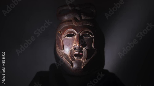 Creepy, masked cultist standing in a dark room. Scary horror scene, mysterious man in a tribal mask isolated on a black background. Eerie mask, devil concept.