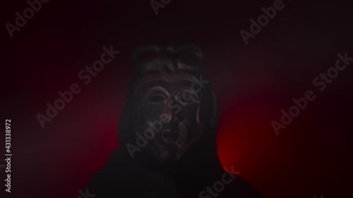 Creepy, masked cultist standing in a dark room. Scary horror scene, mysterious man in a tribal mask isolated on a black background. Eerie mask, devil concept.