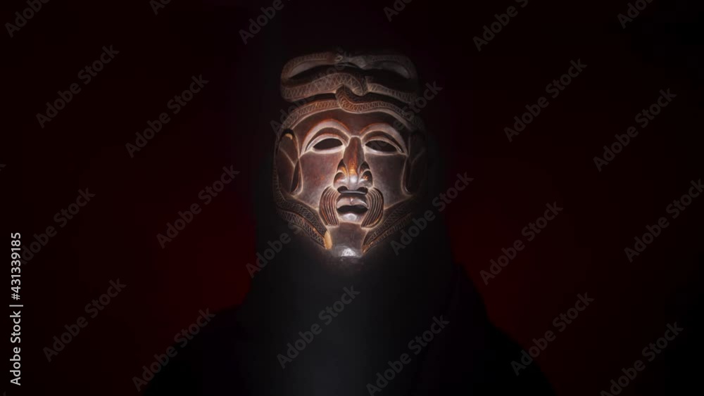 Creepy, masked cultist standing in a dark room. Scary horror scene, mysterious man in a tribal mask isolated on a black background. Eerie mask, devil concept. Creepy, masked cultist standing in a dark room. Scary horror scene, mysterious man in a tribal mask isolated on a black background. Eerie mask, devil concept.