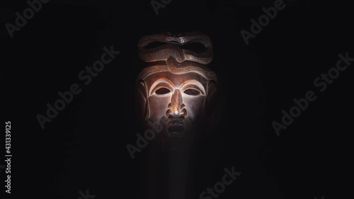 Creepy, masked cultist standing in a dark room. Scary horror scene, mysterious man in a tribal mask isolated on a black background. Eerie mask, devil concept.