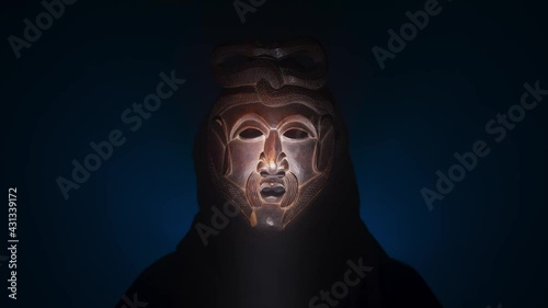 Creepy, masked cultist standing in a dark room. Scary horror scene, mysterious man in a tribal mask isolated on a black background. Eerie mask, devil concept.
