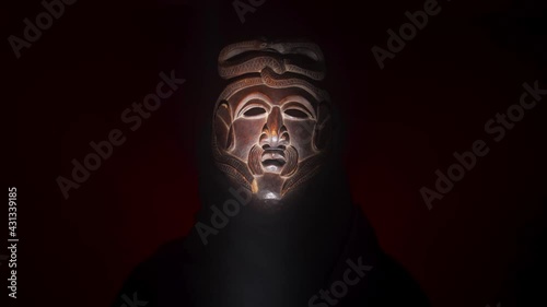 Creepy, masked cultist standing in a dark room. Scary horror scene, mysterious man in a tribal mask isolated on a black background. Eerie mask, devil concept.