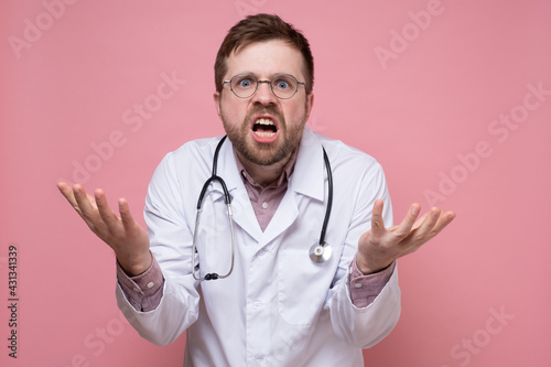 Furious, surprised doctor makes a questioning and bewildered gesture with hands and looks at the camera. © koldunova