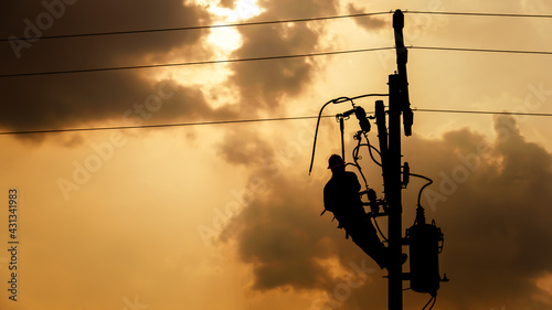 The silhouette of power lineman climbing on an electric pole with a transformer installed. And replacing the damaged hotline clamp, bail clamp, dropout and surge arrester that causes a power failure. photo