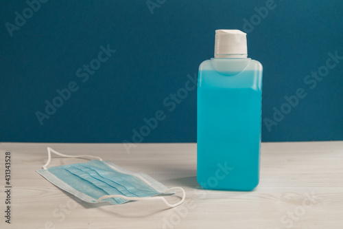 Unlabeled desinfection bottle, blue medical and protective mask on the woods table as a background. prevention of covid- 19, virus and other bacterial.
