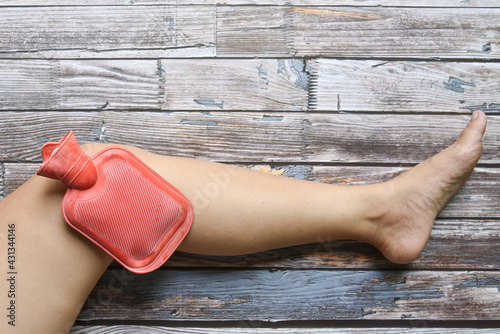 hot red water bottle on woman knee to healing pain on grungy wood, Health care, remedy for pains concept