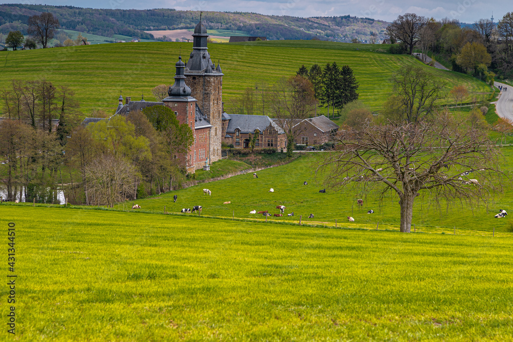 13th century castle in the rolling hill landscape and green meadows in Belgium with winding roads and a dramatic sky.