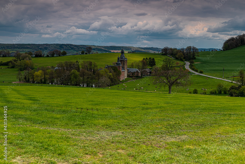 Fototapeta premium 13th century castle in the rolling hill landscape and green meadows in Belgium with winding roads and a dramatic sky.