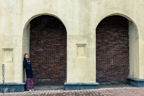 A blonde woman in a black coat stands under an arch © HENADZI BUKA
