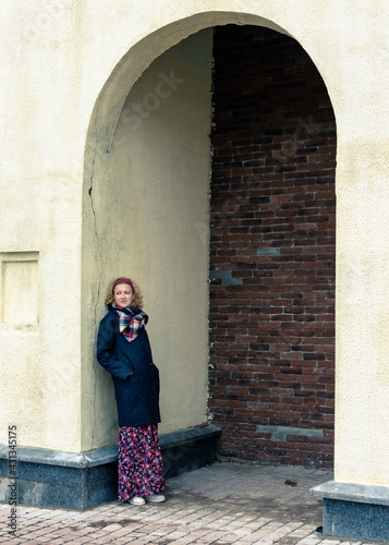 A blonde woman in a black coat stands under an arch