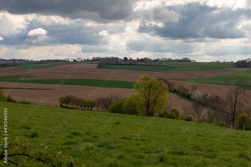 A dramatic cloudscape above the rolling hills in the South of Limburg in the Netherlands. The colourful landscape is split by winding roads and small paths. A dramatic cloudscape above the rolling hills in the South of Limburg in the Netherlands. The colourful landscape is split by winding roads and small paths.