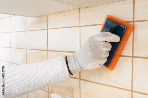 the hands of the master rubbing a brown grout for joints on white tiles with a special sponge, finishing work photo