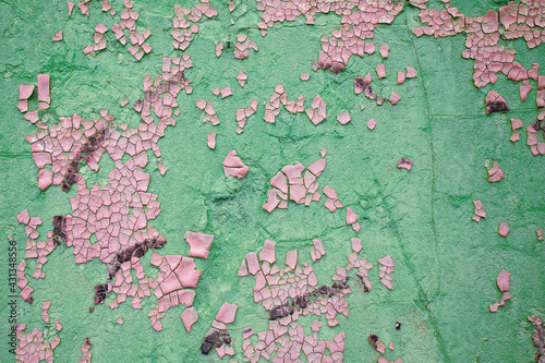 Damaged wall in abstract pink and green colors with peeling paint.