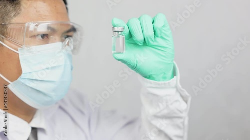 A male doctor, wearing a mask in his hand, has a vaccine to prevent COVID-19, the doctor glances at the vaccine in hopes.