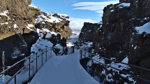 Fotografie Diminishing perspective of snow-covered hiking path leading through Almannagjá gorge in Þingvellir national park, Iceland, a rift valley of Mid-Atlantic Ridge with steep cliffs on sunny winter day
