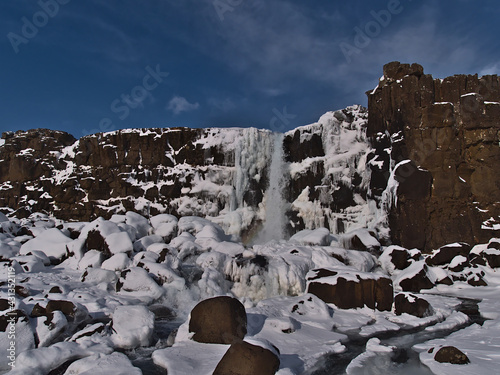 Beautiful front view of Öxarárfoss waterfall in rocky Almannagjá canyon in Þingvellir national park, Golden Circle, Iceland, in winter season with snow and icicles on sunny day. photo