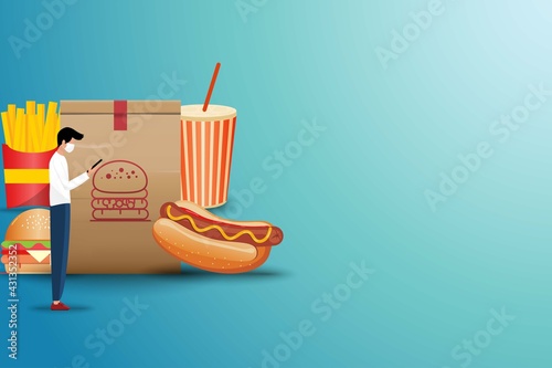 Concept of online fast food delivery service, young man standing in front of a big hamburger bag to order fast food (sparkling water, hot dog, hamburger and french fries) in green color background.