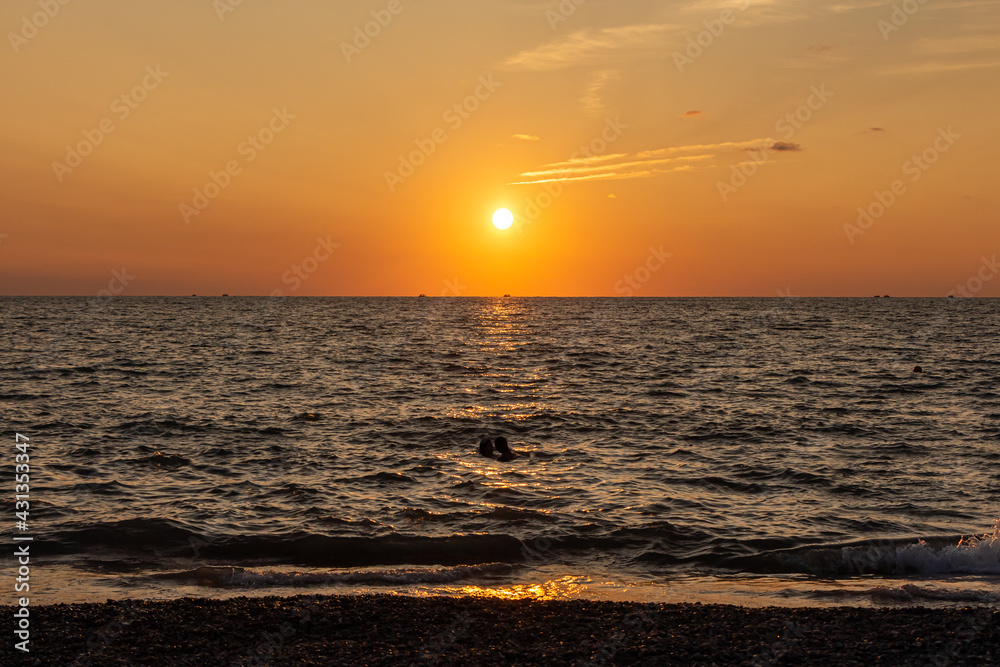 Beautiful orange sunrise is on the beach by the sea with black ship silhouettes and a group of swimming people